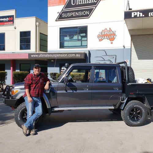Proud customer standing next to his landcruiser in front of Ultimate Suspension workshop
