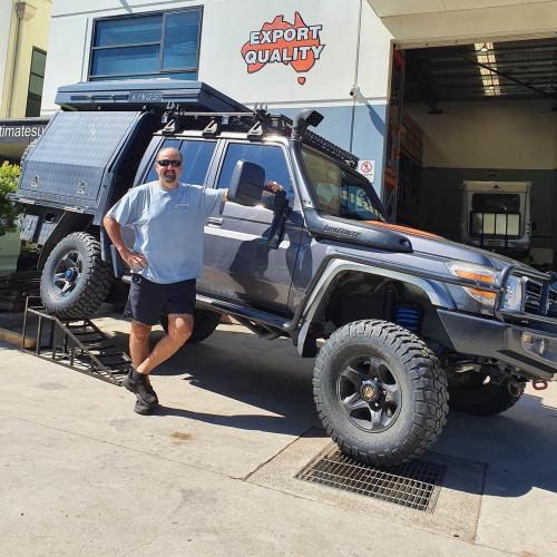 Proud customer standing next to his Landcruiser 79 Series in front of Ultimate Suspension workshop